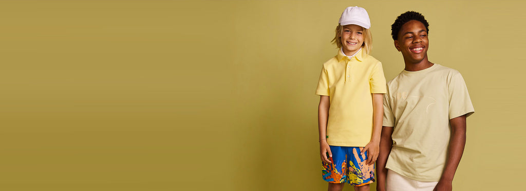 Two happy boys wearing Polo Shirt in yellow, Global Unity Silky Short in Royal Blue, BE Cotton T-Shirt in olive and Everyday Lounge Short in cream by BE.Kids
